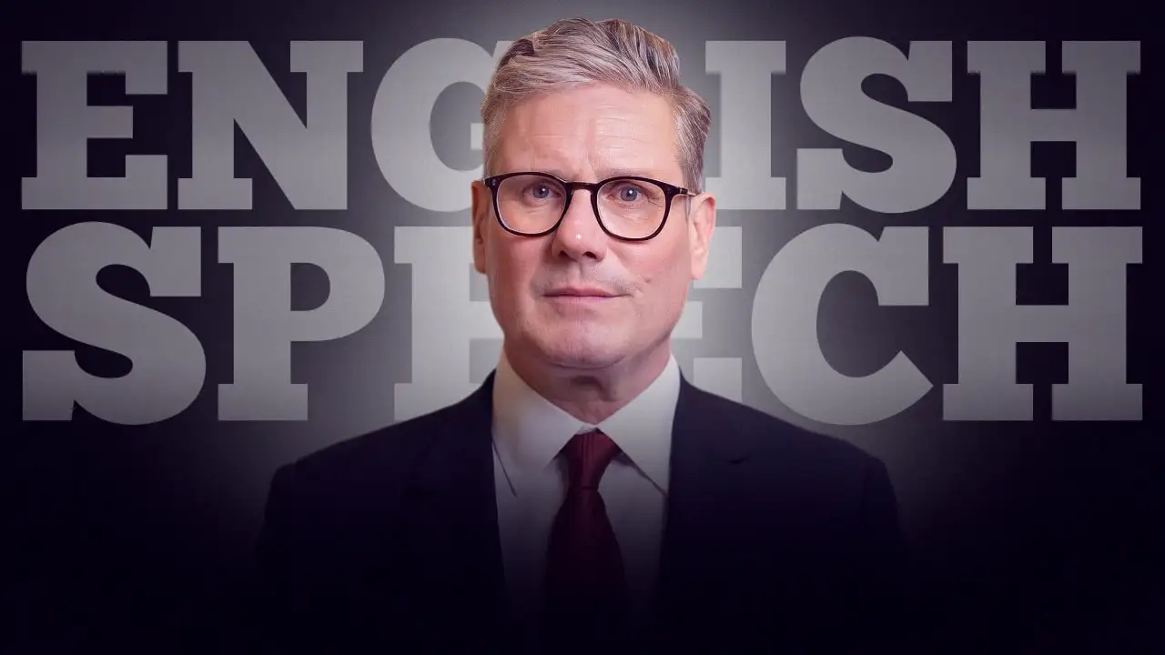 Man in a suit and tie speaking in front of a background with the words "ENGLISH SPEECH."